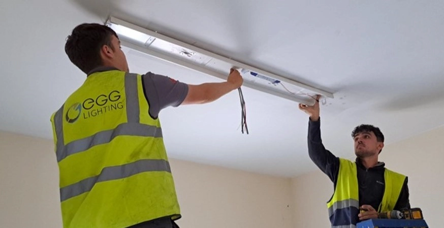 Two EGG electricians maintaining a ceiling-mounted emergency luminaire
